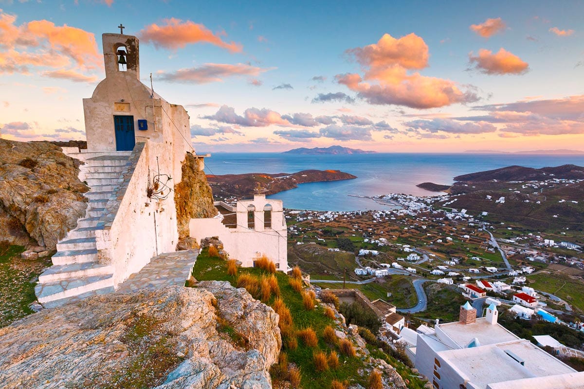 Traditional Greek chapel on a hill overlooking a coastal village in Crete at sunset.