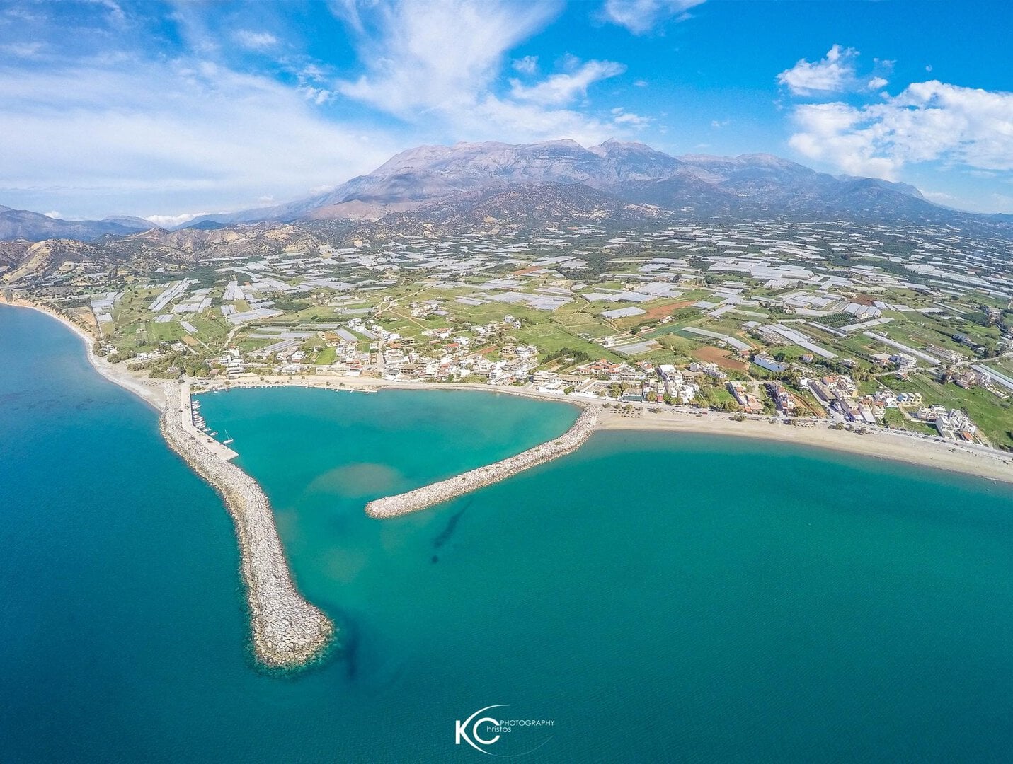 Παραλία και λιμάνι με βράχια και βουνό στο βάθος, θέα από ψηλά.